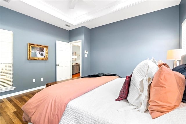 bedroom with a tray ceiling, crown molding, visible vents, wood finished floors, and baseboards