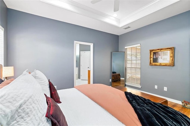 bedroom featuring wood finished floors, visible vents, baseboards, a tray ceiling, and crown molding