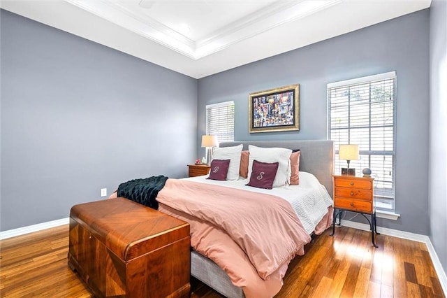 bedroom featuring crown molding, baseboards, a raised ceiling, and hardwood / wood-style floors