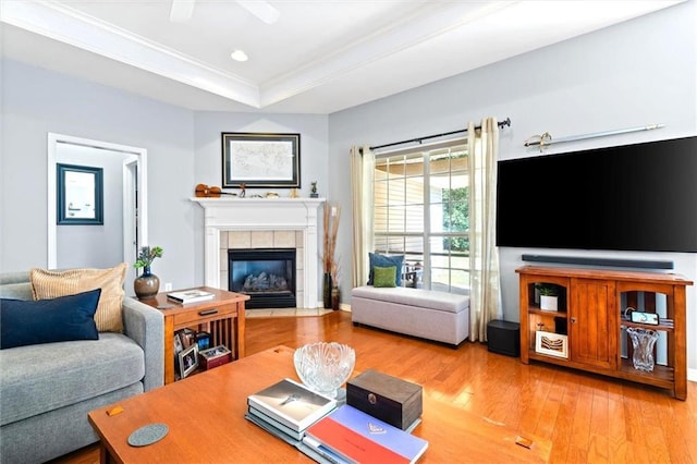 living area with a tile fireplace, light wood-style flooring, recessed lighting, a raised ceiling, and crown molding