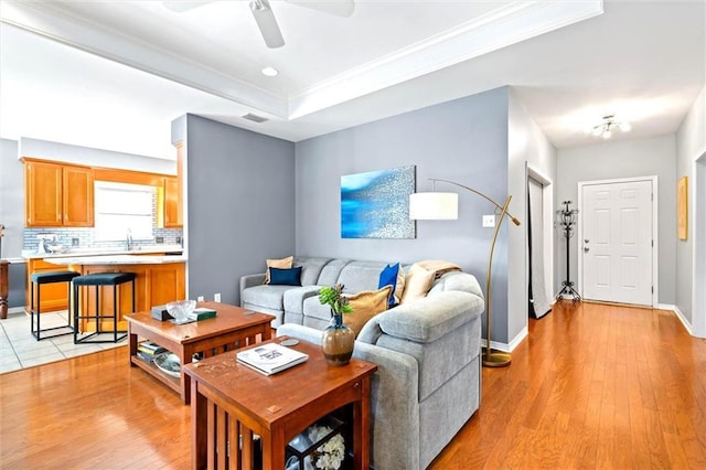 living room featuring a raised ceiling, visible vents, ceiling fan, light wood-type flooring, and baseboards