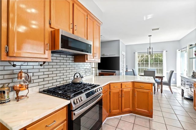 kitchen with light tile patterned floors, stainless steel appliances, light countertops, decorative backsplash, and a peninsula