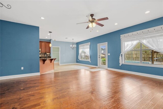 unfurnished living room with ceiling fan with notable chandelier, light hardwood / wood-style floors, and sink