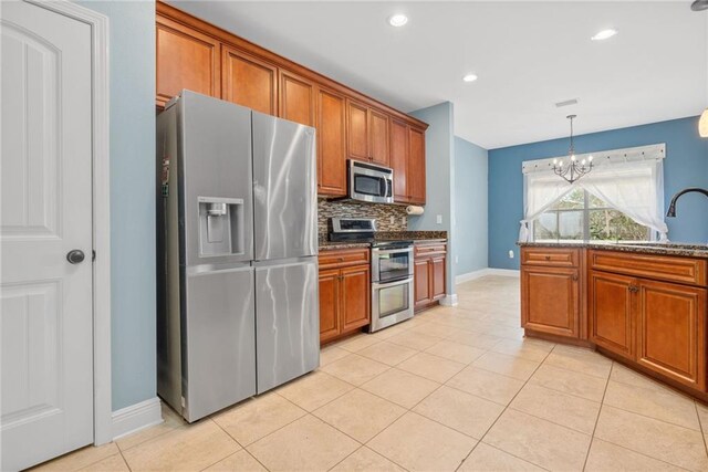 kitchen with a chandelier, sink, hanging light fixtures, stainless steel appliances, and dark stone countertops