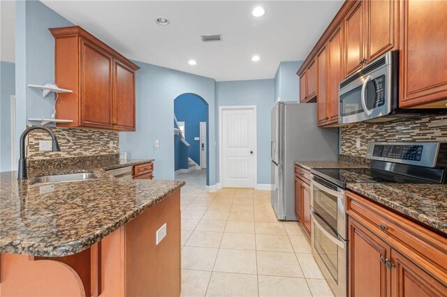 kitchen featuring decorative backsplash, stainless steel appliances, dark stone countertops, and sink