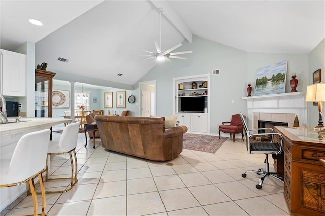 living room featuring lofted ceiling with beams, a tiled fireplace, light tile patterned floors, ceiling fan, and built in shelves