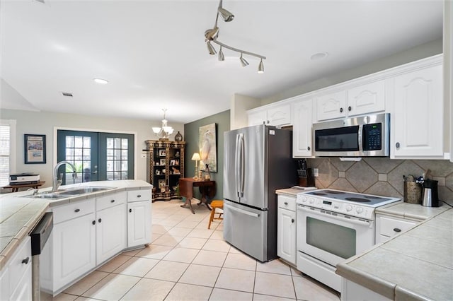 kitchen with sink, appliances with stainless steel finishes, white cabinetry, tasteful backsplash, and tile counters