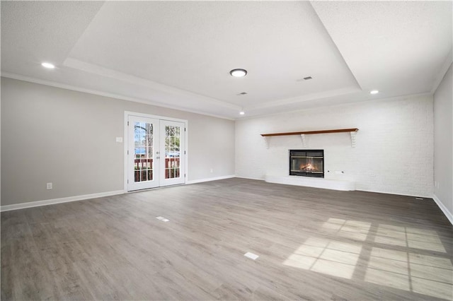 unfurnished living room with a glass covered fireplace, a raised ceiling, wood finished floors, and french doors