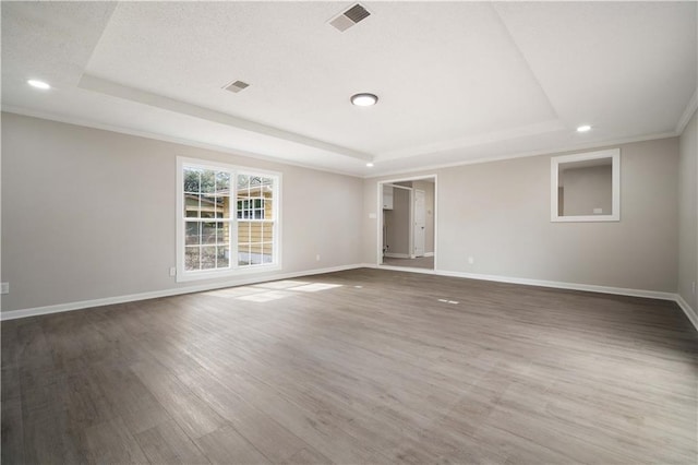 empty room with a tray ceiling, wood finished floors, visible vents, and baseboards