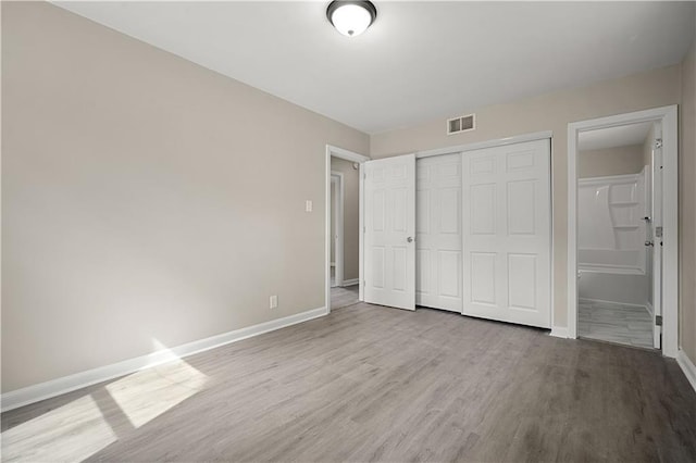 unfurnished bedroom featuring baseboards, visible vents, connected bathroom, wood finished floors, and a closet