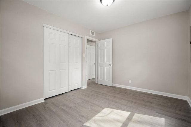 unfurnished bedroom featuring a closet, visible vents, baseboards, and wood finished floors