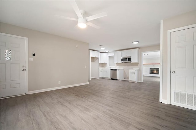 unfurnished living room featuring a ceiling fan, baseboards, visible vents, and wood finished floors