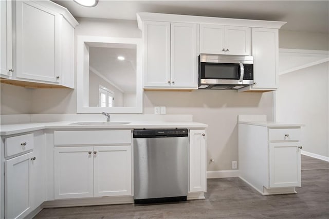 kitchen with stainless steel appliances, white cabinets, a sink, and wood finished floors