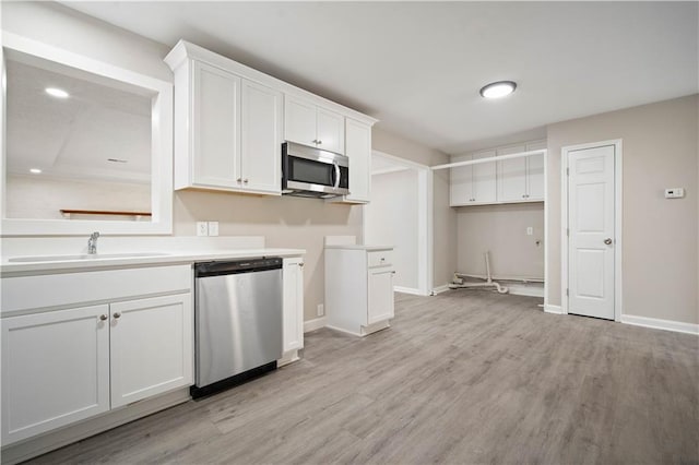 kitchen with stainless steel appliances, light wood-style floors, white cabinets, a sink, and baseboards