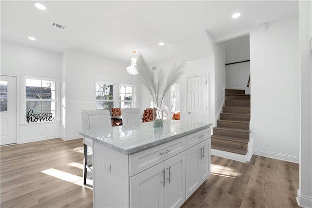 kitchen featuring a breakfast bar, white cabinets, light hardwood / wood-style flooring, a kitchen island, and light stone counters