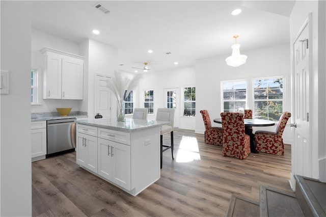 kitchen featuring light stone countertops, stainless steel dishwasher, wood-type flooring, a center island, and white cabinetry