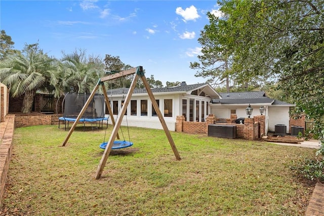 rear view of property featuring a yard, a trampoline, central AC, and a sunroom