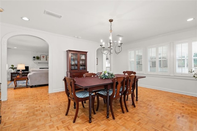 dining room featuring a brick fireplace, a chandelier, crown molding, and light parquet flooring