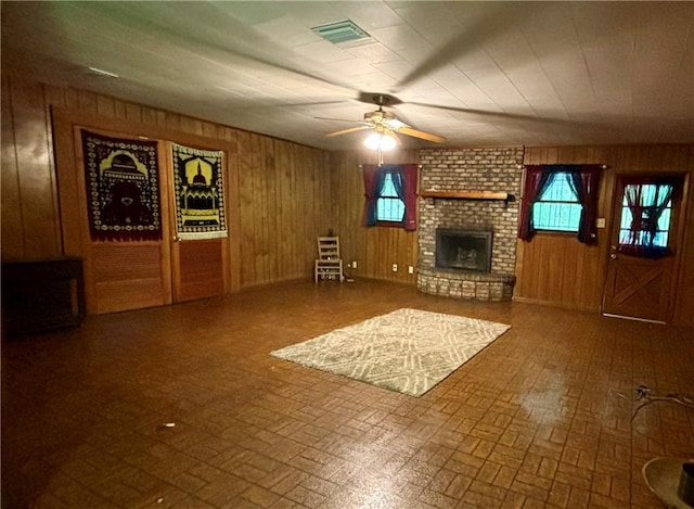 unfurnished living room with brick wall, a brick fireplace, wooden walls, and ceiling fan