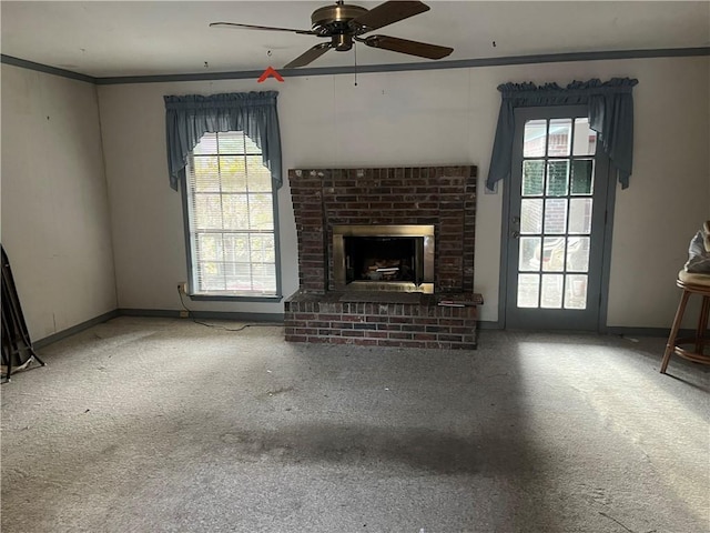 unfurnished living room with ceiling fan, ornamental molding, carpet floors, and a brick fireplace