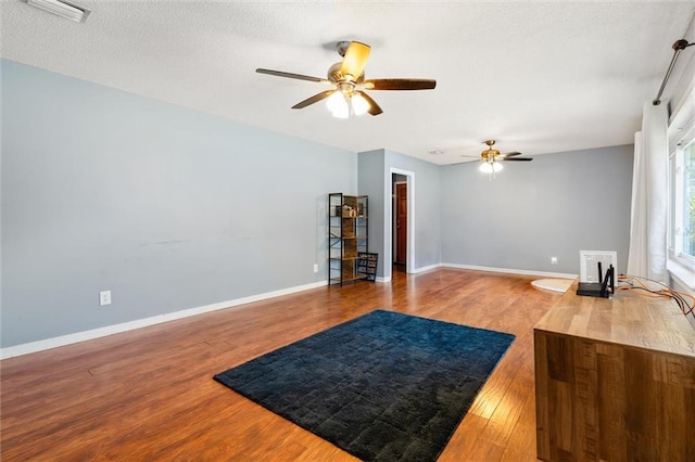 living room featuring a ceiling fan, visible vents, wood finished floors, baseboards, and a textured ceiling