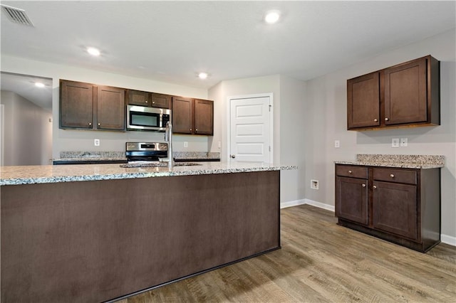 kitchen with stove, sink, dark brown cabinets, light stone counters, and wood-type flooring