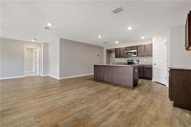 kitchen featuring appliances with stainless steel finishes, dark brown cabinets, a kitchen island with sink, sink, and hardwood / wood-style floors