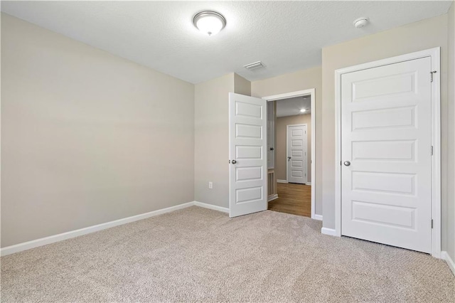 unfurnished bedroom featuring light colored carpet, a textured ceiling, and a closet