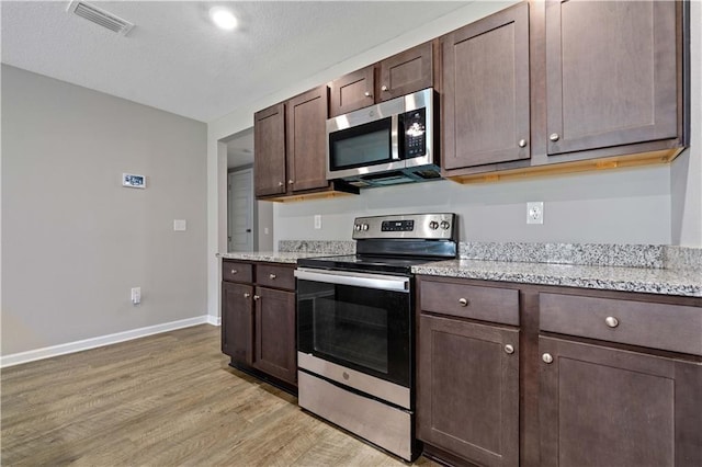 kitchen with light stone countertops, dark brown cabinets, stainless steel appliances, and light hardwood / wood-style flooring