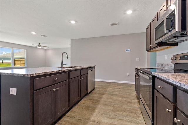 kitchen with a kitchen island with sink, sink, ceiling fan, appliances with stainless steel finishes, and light hardwood / wood-style floors