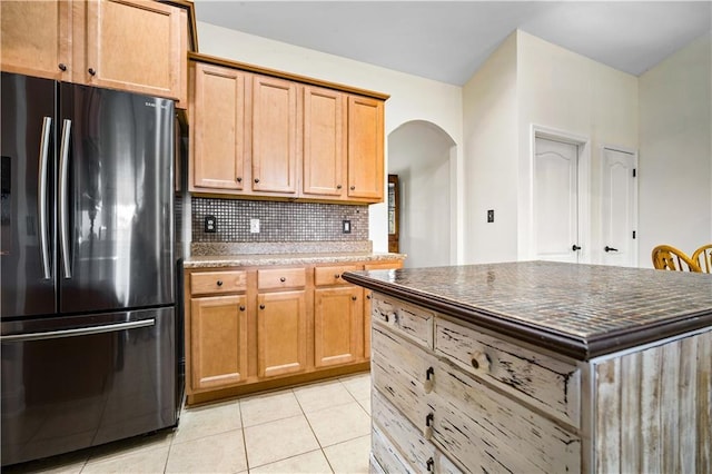 kitchen with backsplash, stainless steel fridge, light tile patterned floors, and a kitchen island