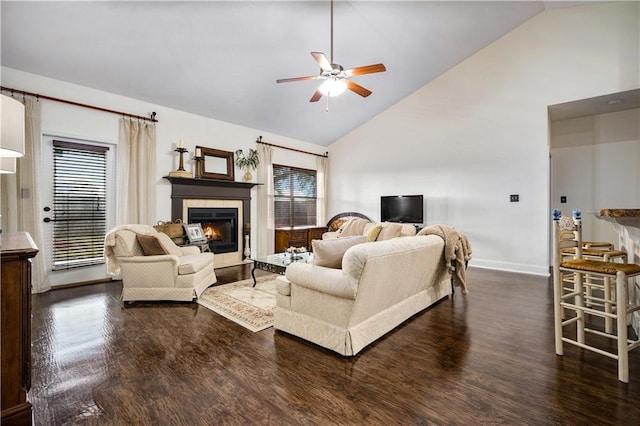 living room with high vaulted ceiling, ceiling fan, dark wood-type flooring, and a tiled fireplace