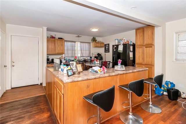 kitchen with dark wood-type flooring, black refrigerator with ice dispenser, a breakfast bar, and brown cabinetry