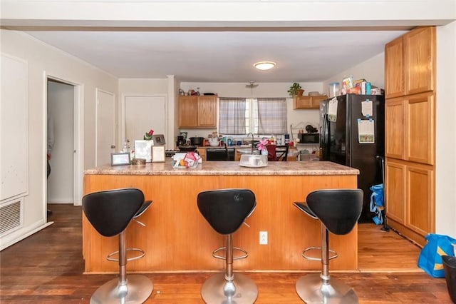 kitchen featuring visible vents, black appliances, a kitchen breakfast bar, and wood finished floors