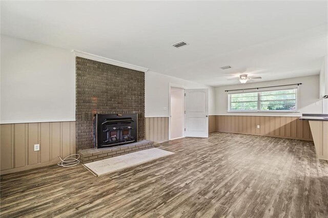 unfurnished living room featuring hardwood / wood-style floors, a fireplace, wooden walls, and ceiling fan