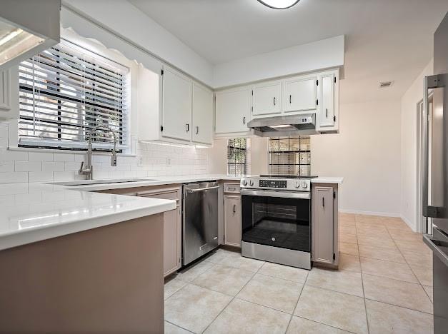 kitchen with sink, kitchen peninsula, appliances with stainless steel finishes, light tile patterned floors, and backsplash