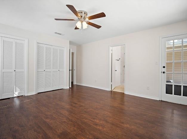 unfurnished bedroom featuring ensuite bath, ceiling fan, multiple closets, and dark hardwood / wood-style flooring