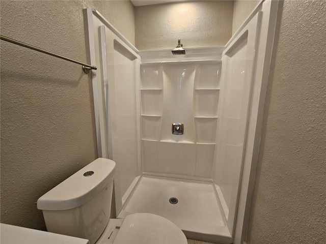 full bathroom with toilet, a textured wall, and a shower stall
