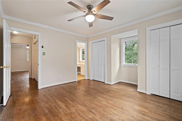 unfurnished bedroom with multiple closets, ceiling fan, crown molding, and wood-type flooring