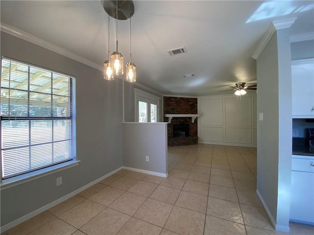 interior space with light tile patterned floors, crown molding, ceiling fan with notable chandelier, and a brick fireplace