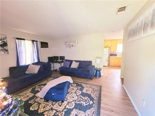 living room featuring light wood-type flooring, visible vents, a textured ceiling, and baseboards