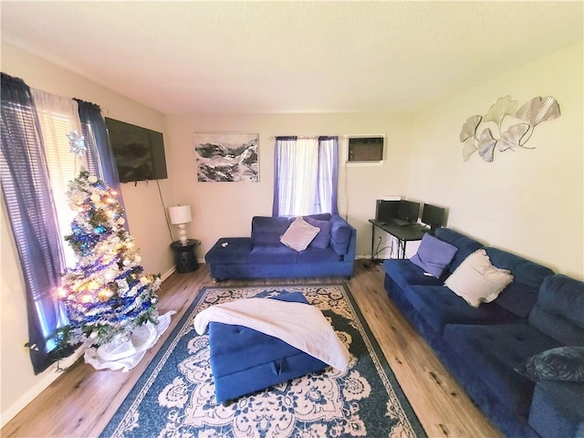 living area with a healthy amount of sunlight, a wall mounted AC, and wood finished floors