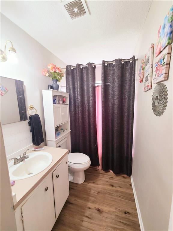 bathroom featuring toilet, wood finished floors, vanity, visible vents, and backsplash