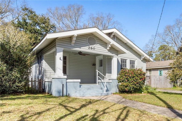 bungalow-style house with a front lawn, fence, and ceiling fan