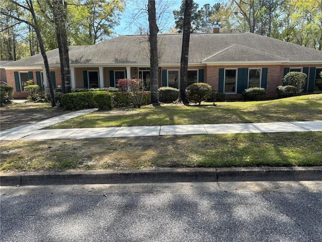 ranch-style home featuring a chimney, a shingled roof, and a front lawn