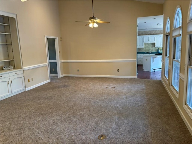 unfurnished room with a ceiling fan, a sink, baseboards, and dark carpet