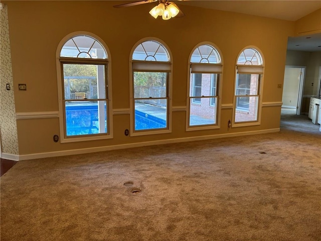 carpeted spare room featuring baseboards and ceiling fan