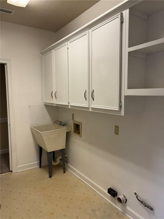 laundry area with light floors, a textured ceiling, baseboards, cabinet space, and hookup for a washing machine