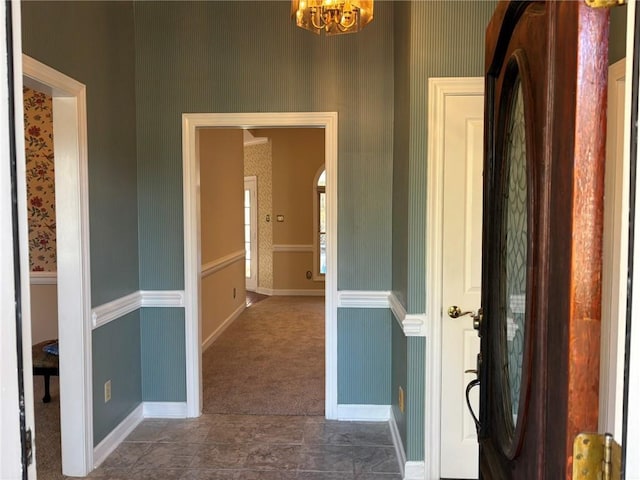 hall with baseboards, wallpapered walls, arched walkways, carpet floors, and a notable chandelier