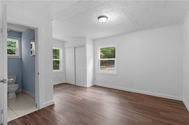 unfurnished bedroom with baseboards, ensuite bathroom, a closet, and dark wood finished floors